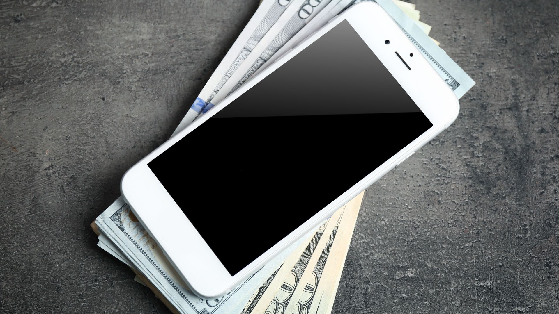 A smart phone sitting on top of a pile of money